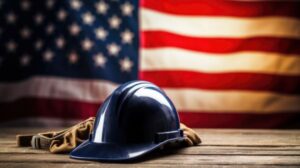 Blue hard hat and work gloves on a wooden table with U.S. flag in the background